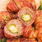 Juicy bacon wrapped cheese filled jalapenos on a plate with one cut open
