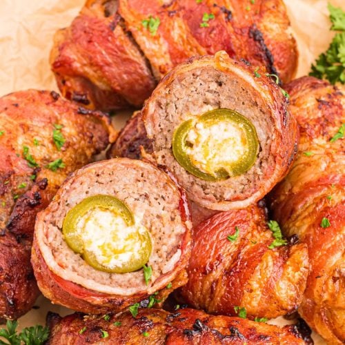 Juicy bacon wrapped cheese filled jalapenos on a plate with one cut open