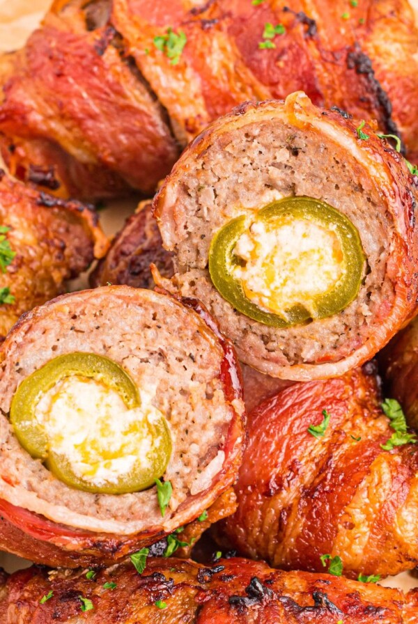 Juicy bacon wrapped cheese filled jalapenos on a plate with one cut open