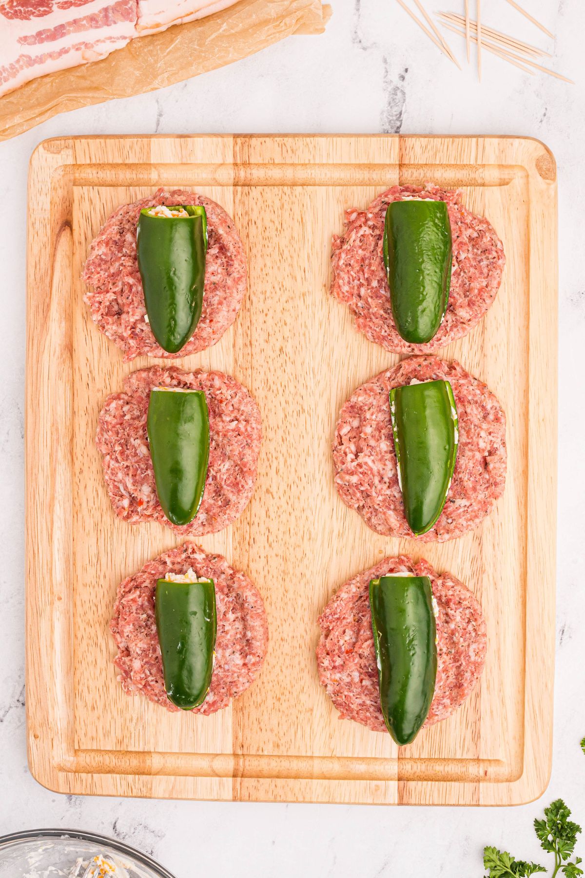 Stuffed jalapenos being wrapped in ground sausage