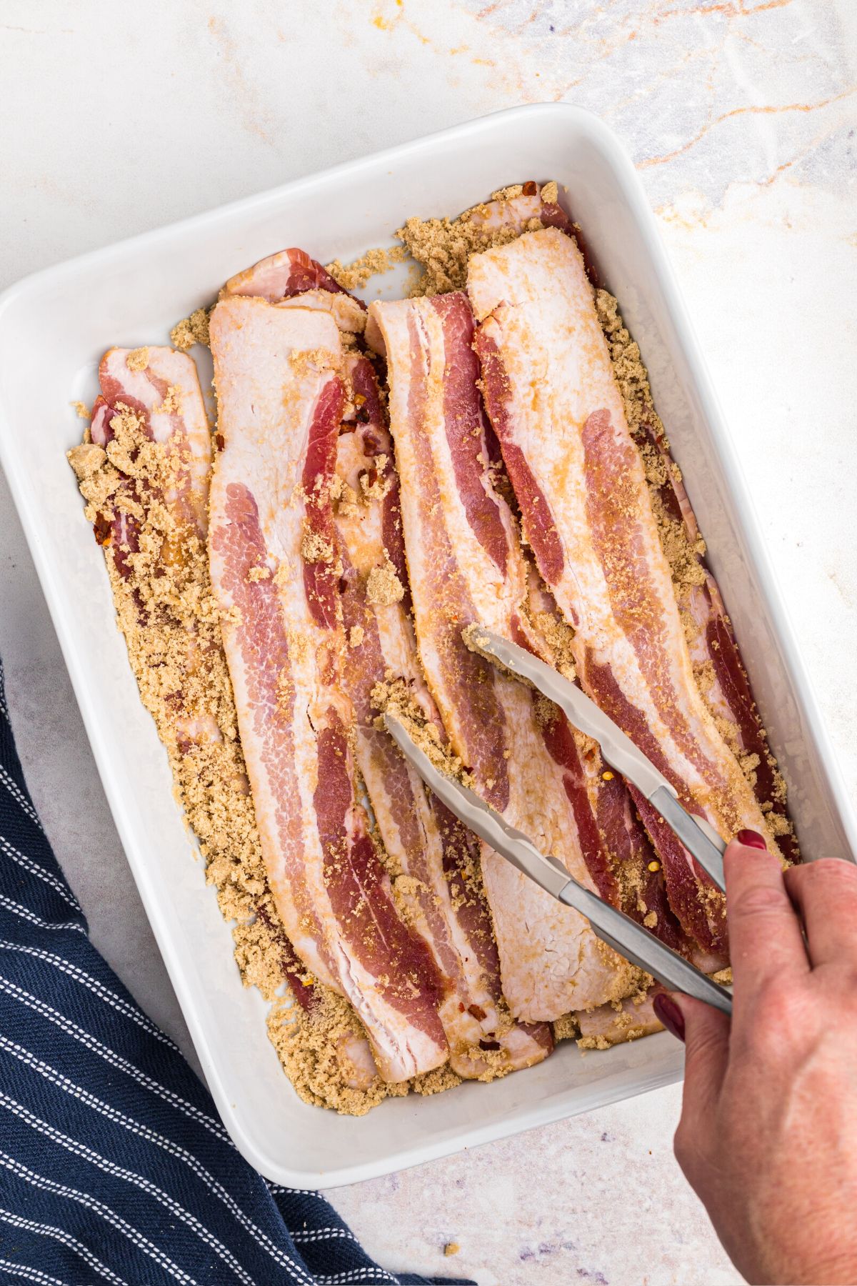 Uncooked thick bacon slices being tossed with brown sugar