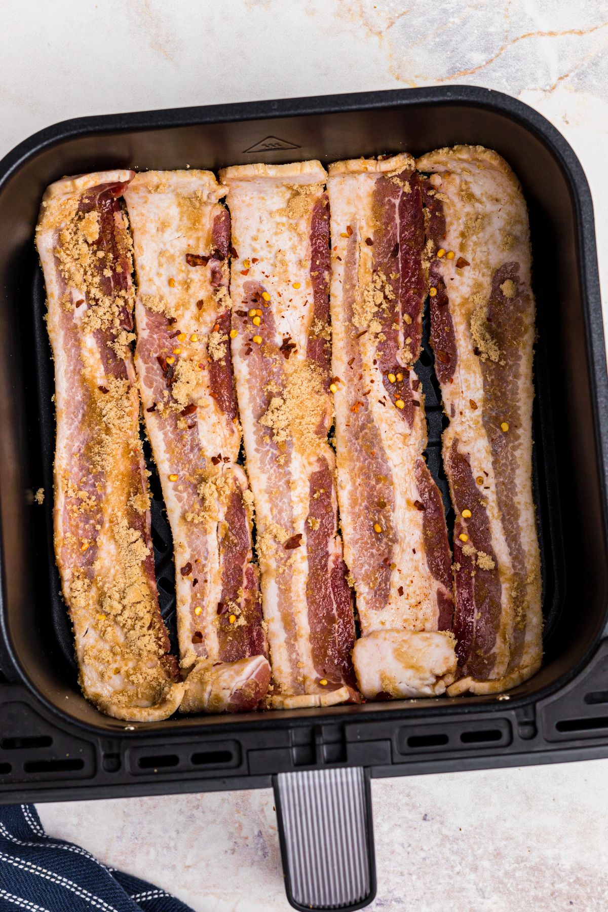 Brown sugar coated thick bacon slices in an air fryer basket.