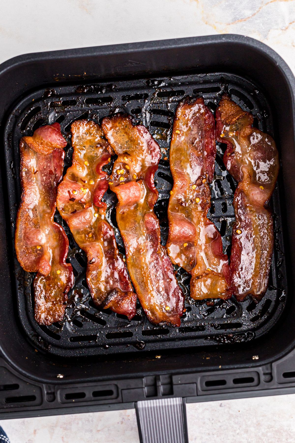 Crispy candied bacon in the air fryer basket after being cooked.