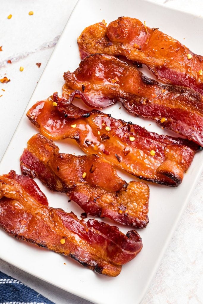 Crispy and juicy carnalized bacon slices on a white plate