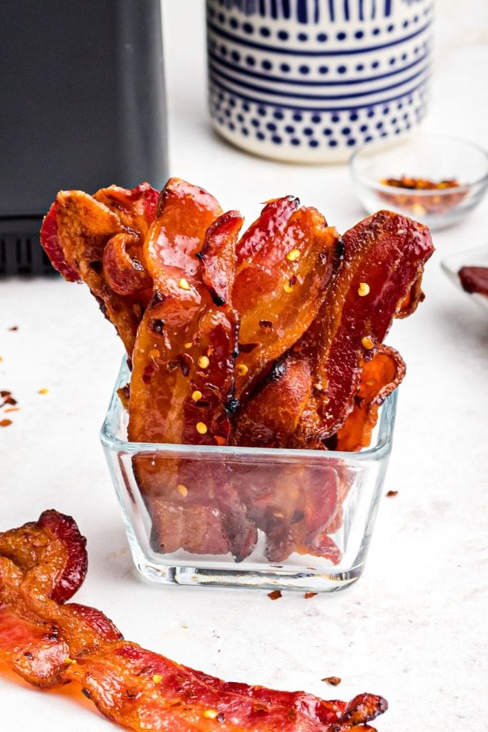 Golden crispy candy bacon in a glass dish in front of the air fryer. 