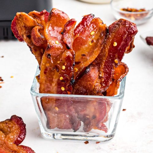 Crispy juicy candied bacon in a clear glass jar.