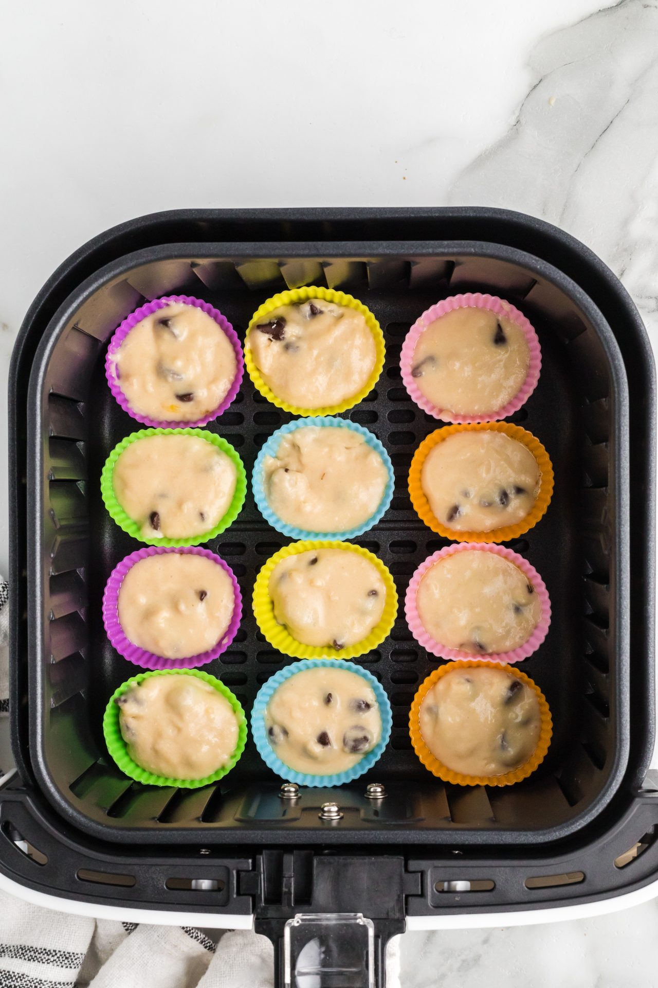 A picture of the colorful silicon cups filled ⅔ of the way up, placed in a single layer in the air fryer basket, and ready to cook.
