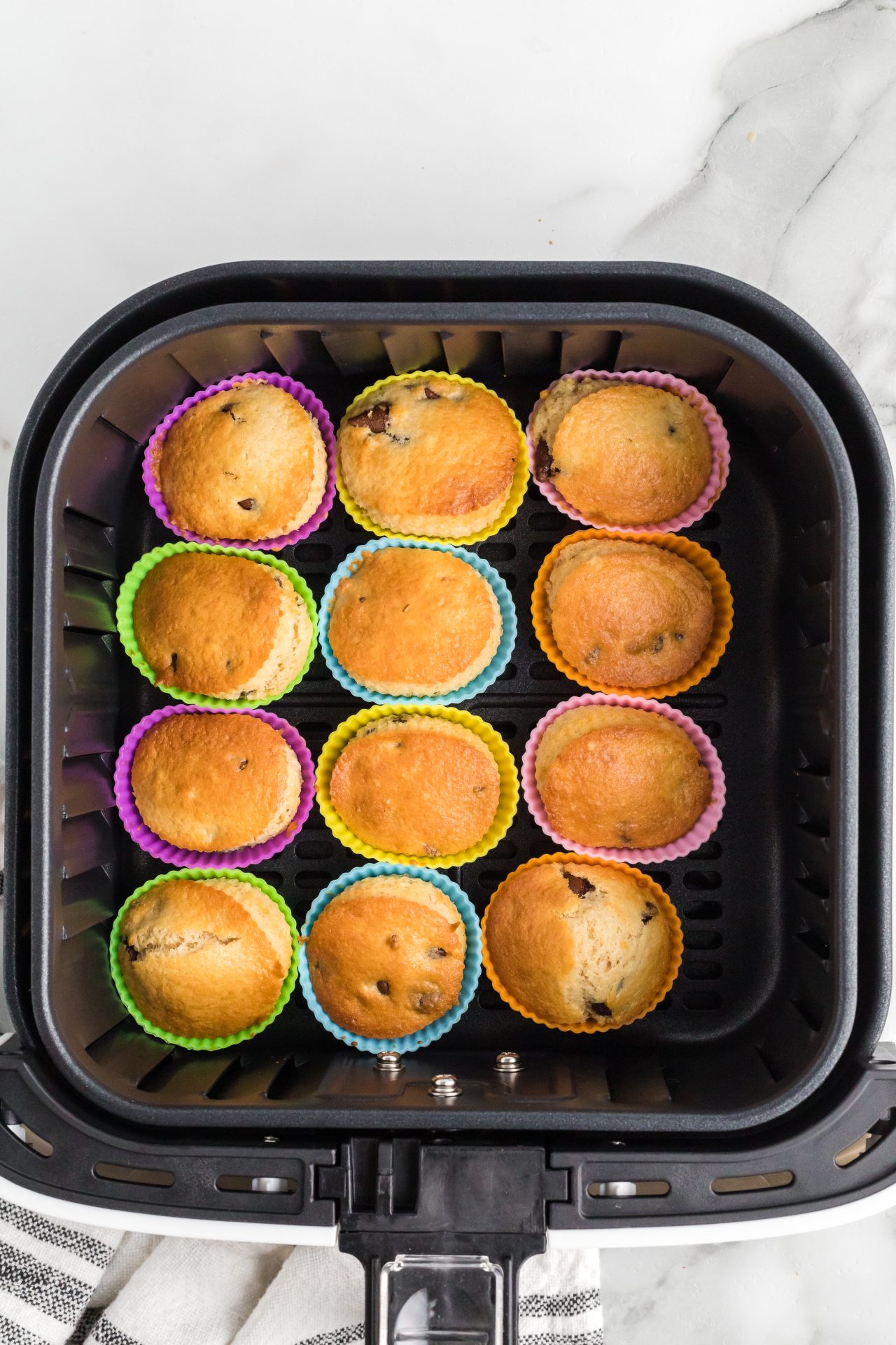 A picture of multicolor silicon cups with fully cooked chocolate chip muffins in the air fryer basket.