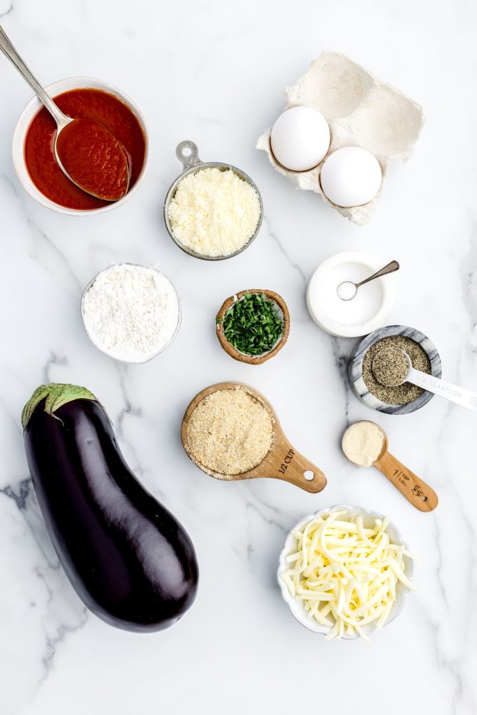 Ingredients needed to make eggplant parmesan measured out on a white marble table. 