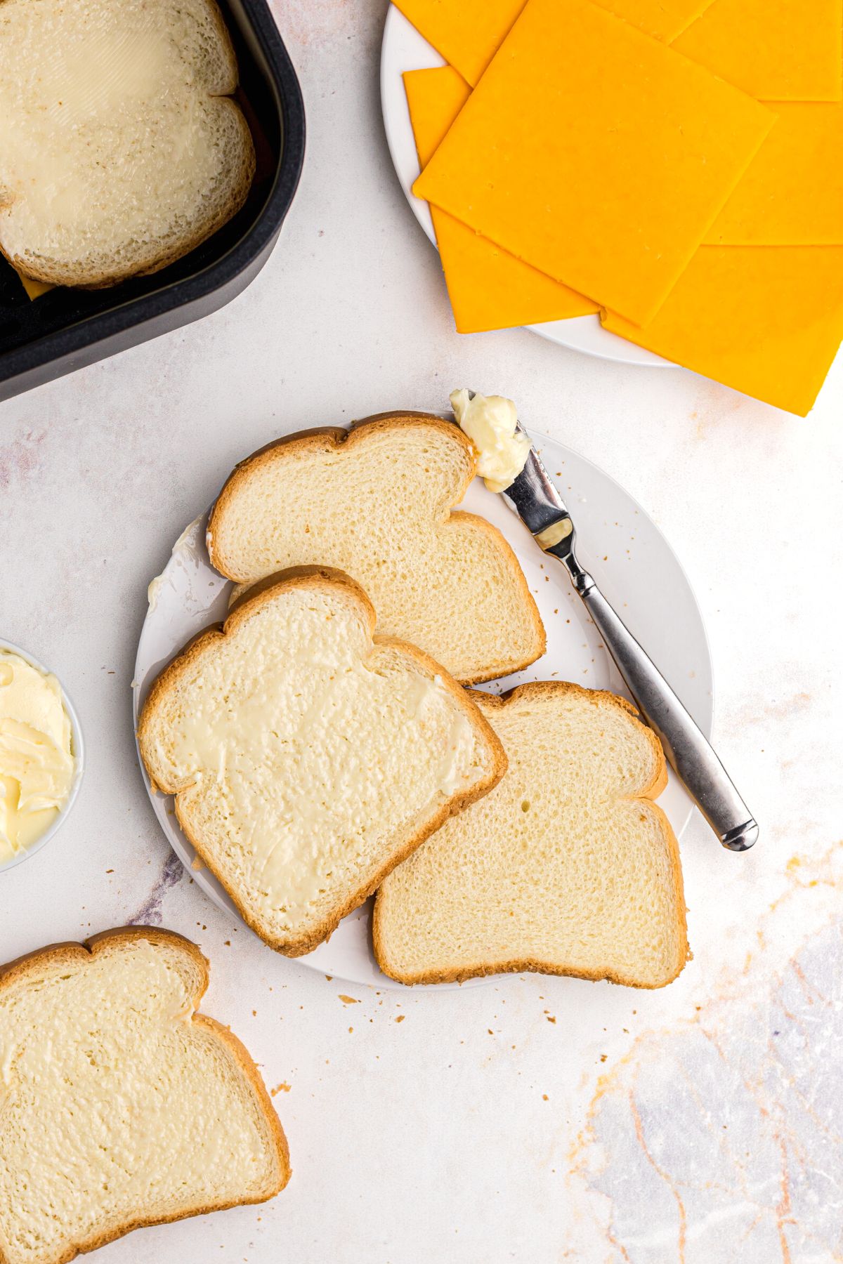 Slices of bread being buttered, then topped with slice of cheese, placed in the air fryer. 