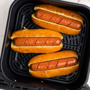 Juicy hot dogs in golden toasted buns in the air fryer basket