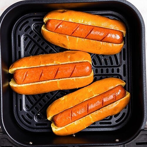 Juicy brown hot dogs in buns in the air fryer basket.