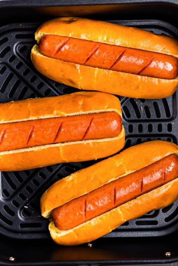 Juicy brown hot dogs in buns in the air fryer basket.