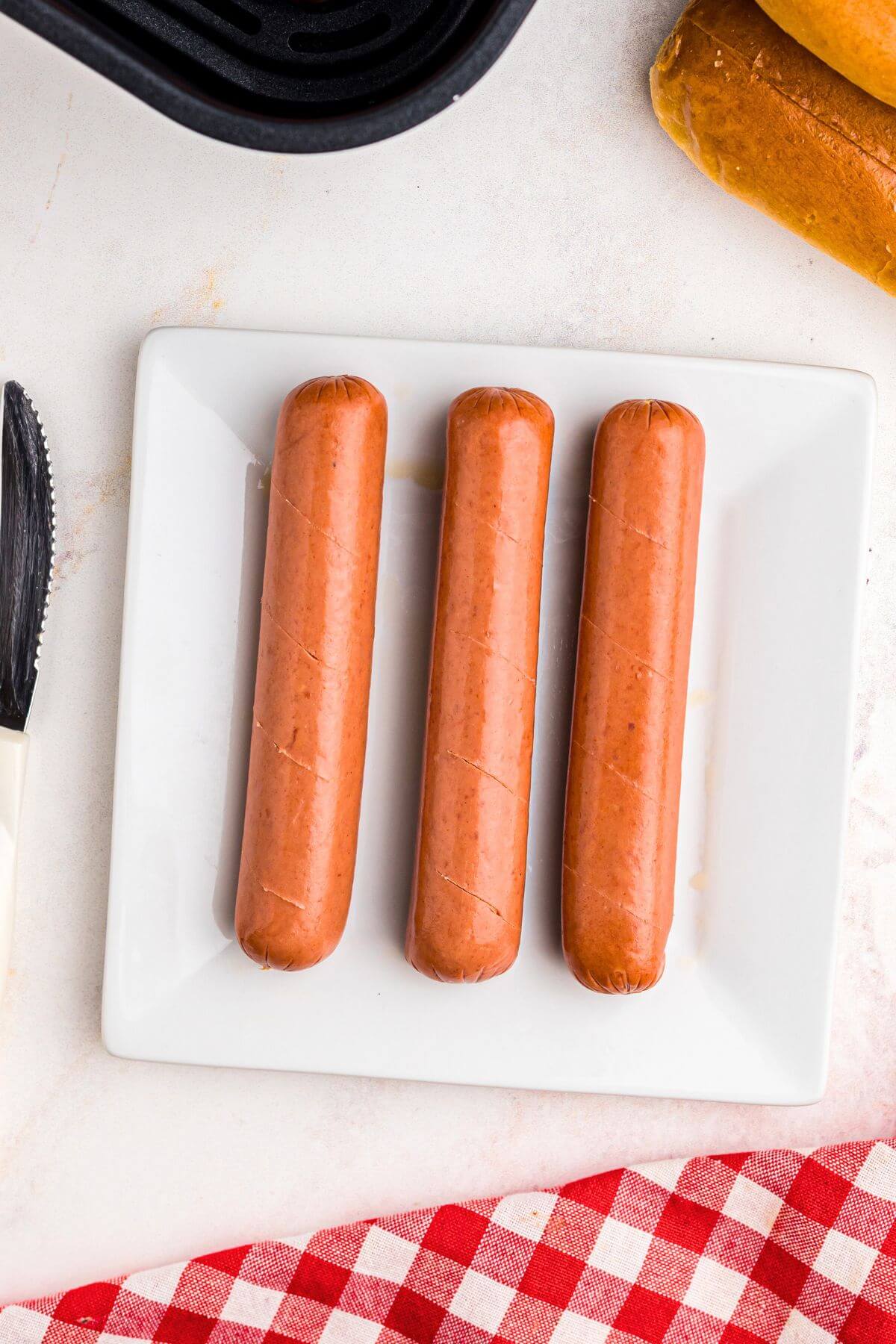 Uncooked hot dogs with slits cut into them on a white plate. 