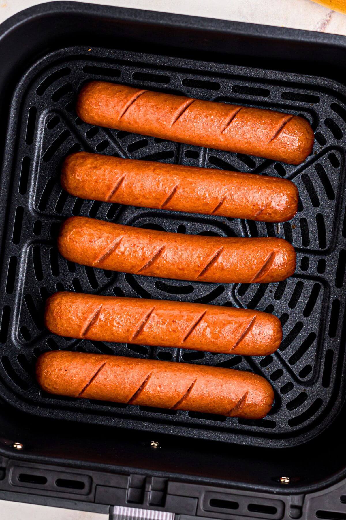 Juicy brown hot dogs in the air fryer basket after being cooked. 