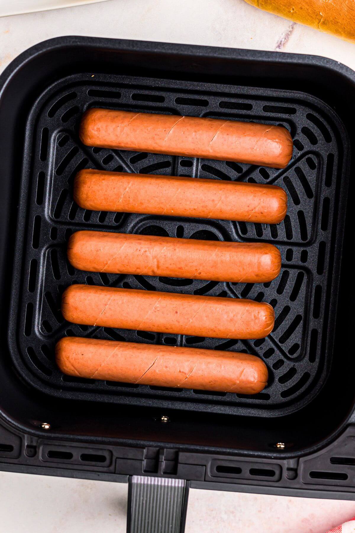 Uncooked hot dogs in the air fryer basket. 