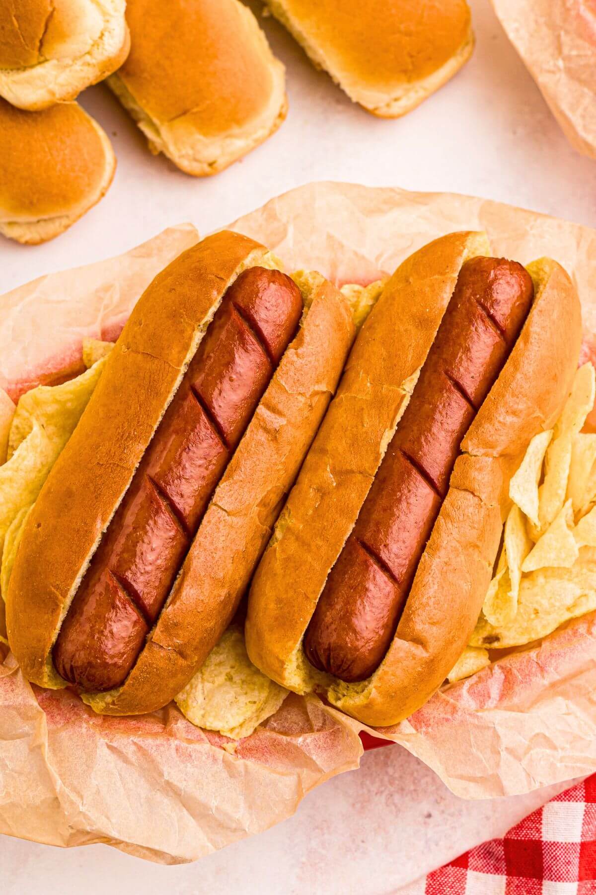 Golden juicy hot dogs in buns, with potato chips next to them. 