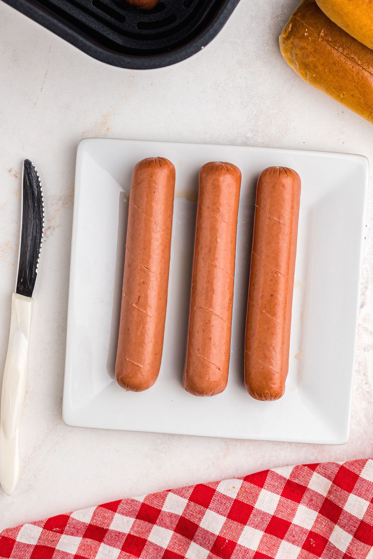 Uncooked hot dogs on a white plate with slits cut into them with a knife