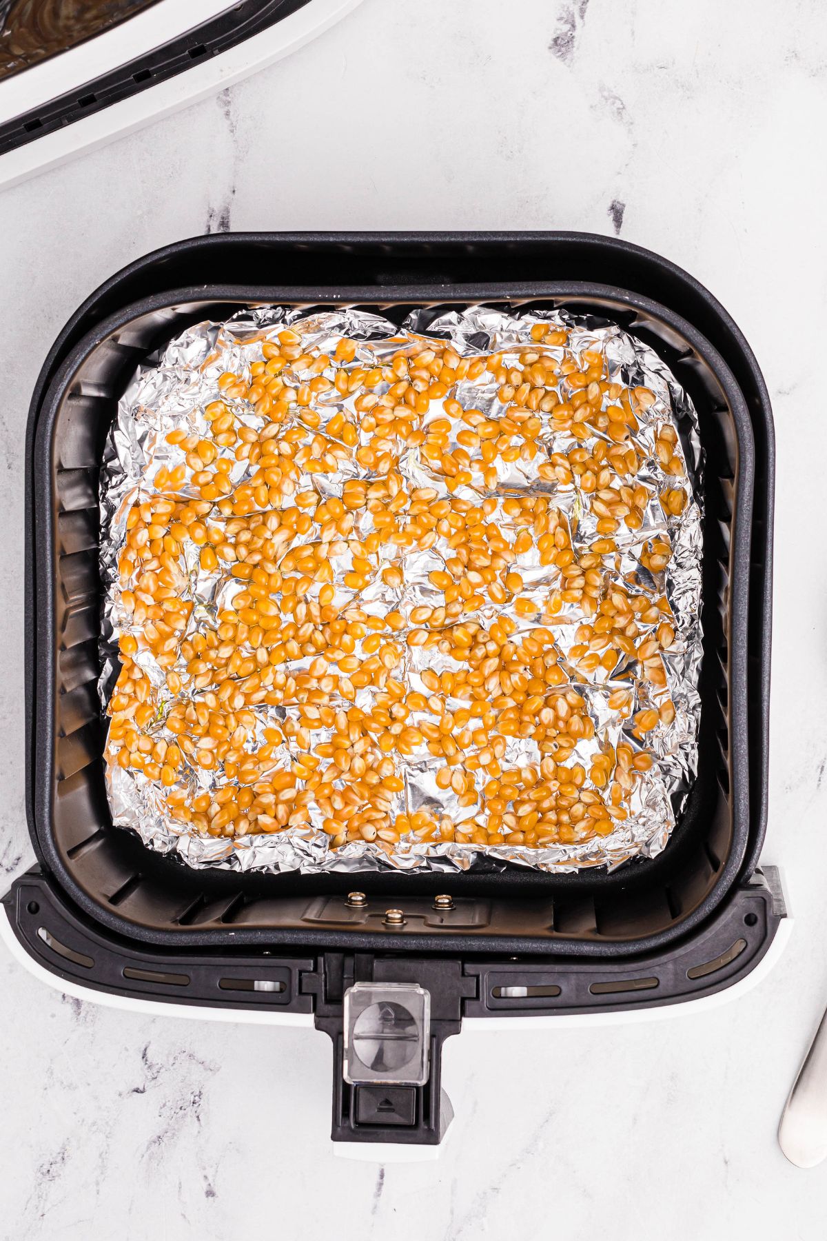 Unpopped kernals in the air fryer basket on top of foil
