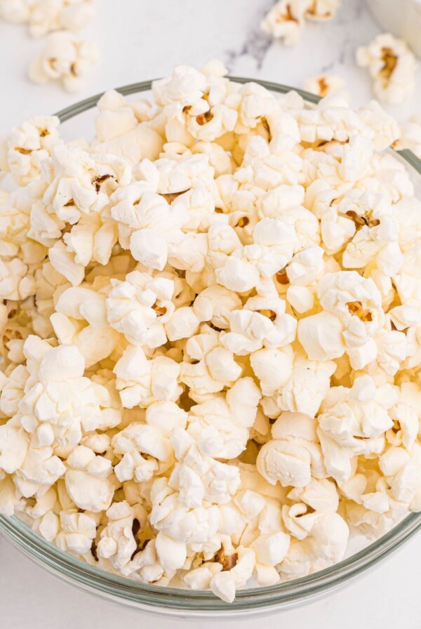 Clear glass bowl filled with fluffy popcorn and a small bowl of melted butter on a marble table.