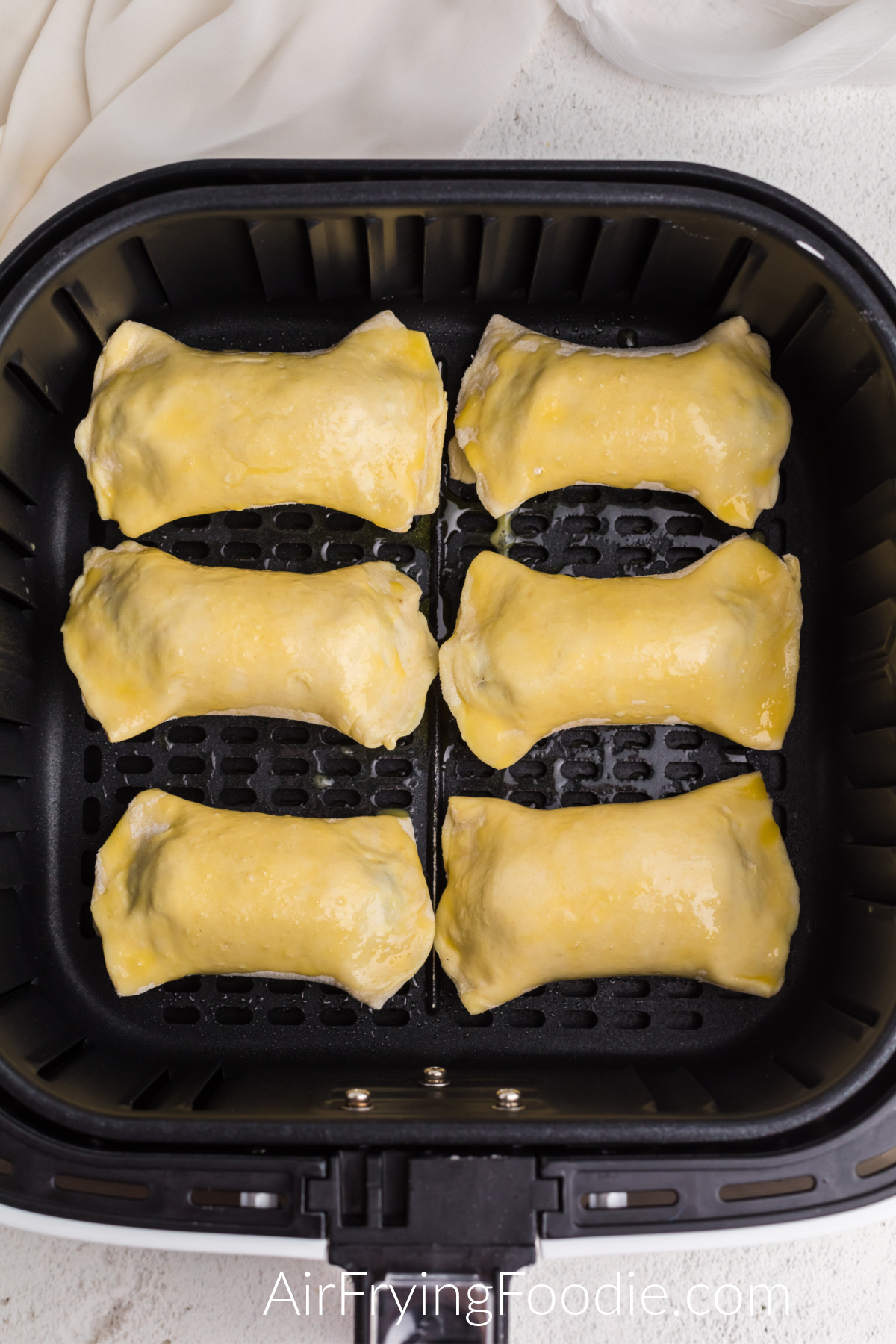 Sausage rolls brushed with egg and placed in a single layer in the basket of the air fryer.