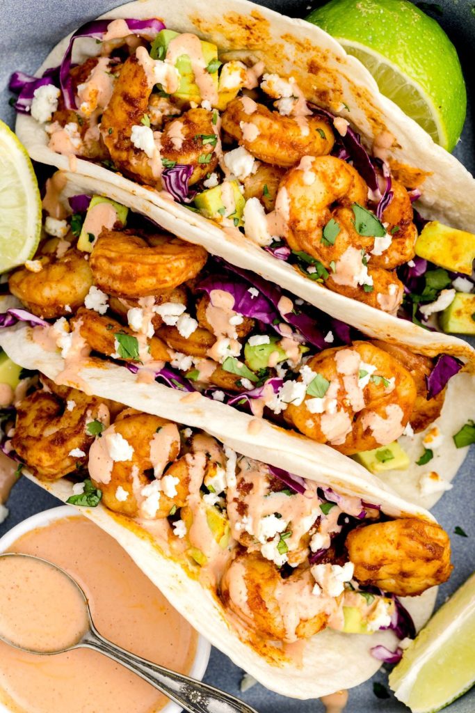 Shrimp tacos put into a pan with sauce and lime wedges.