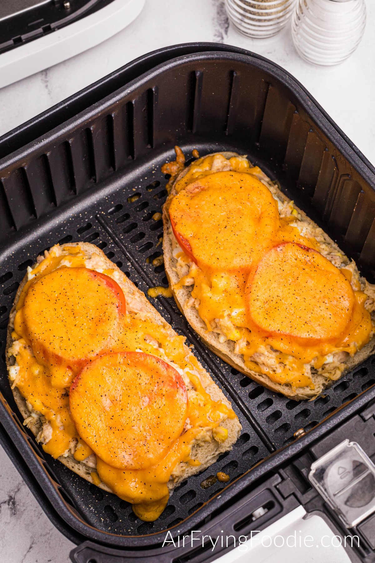 A close-up picture of a tuna melt in the air fryer basket with cheese melted on top.