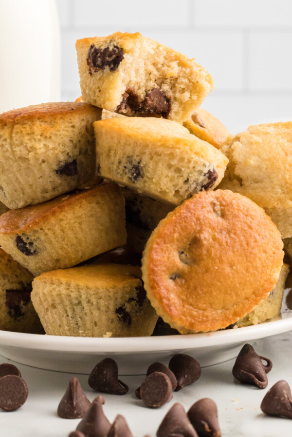 Round white plate fully stacked with chocolate chip air fryer muffins baked in the air fryer with chocolate chips sprinkled around on the table in front of the plate.