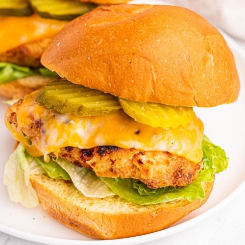 Air fryer copycat chick fil a sandwich dressed with pickles, cheese, lettuce, and sauce and served on a round white plate.