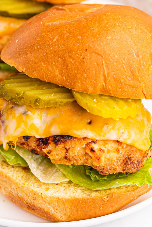 Air fryer copycat chick fil a sandwich dressed with pickles, cheese, lettuce, and sauce and served on a round white plate.