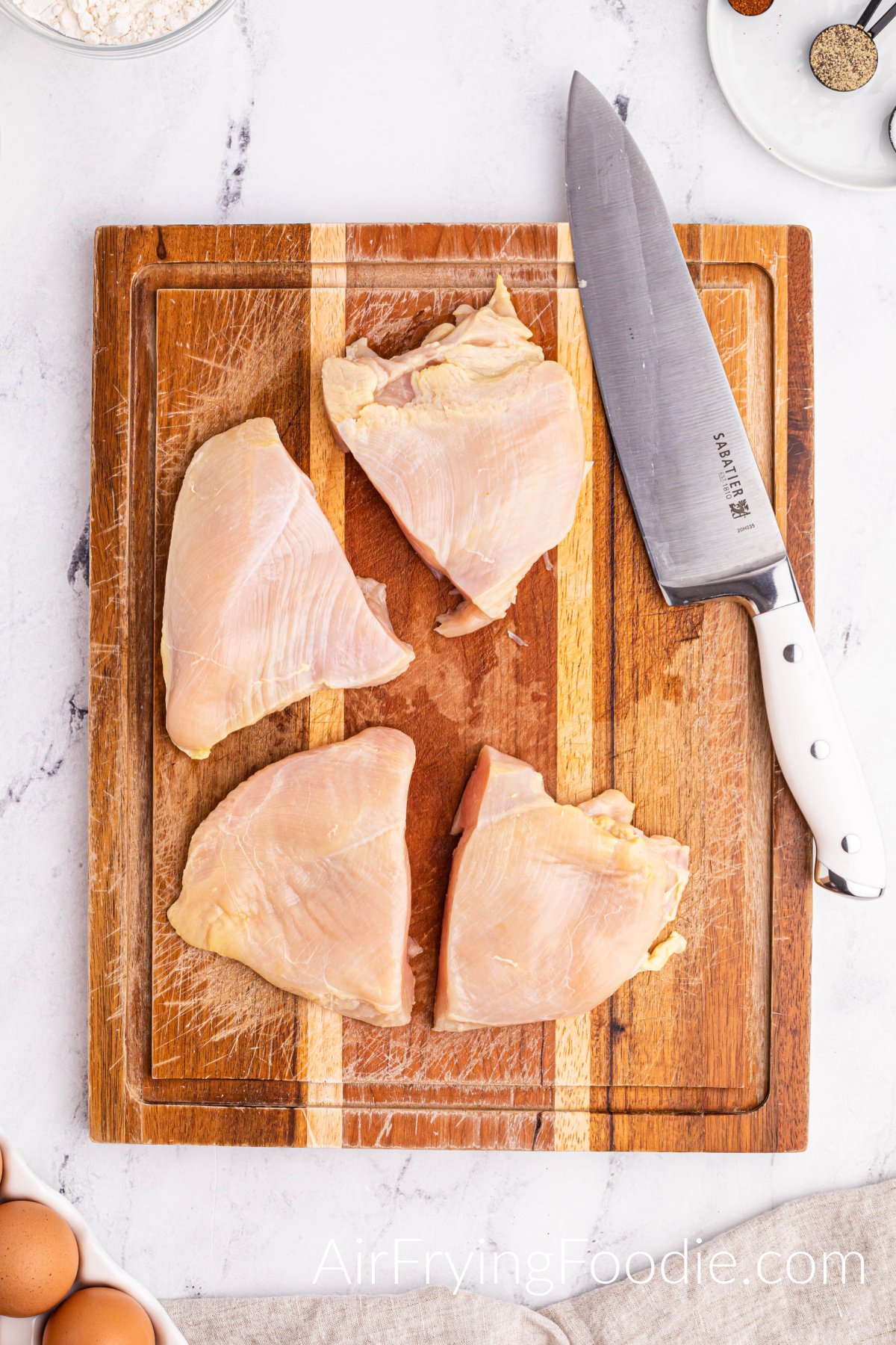A picture of the two raw chicken breasts on a cutting board cut in half with a knife lying on the cutting board at an angle.