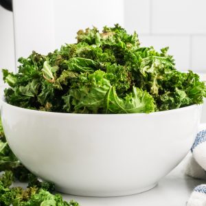 Kale chips are fully cooked in the air fryer and served in a round white bowl.