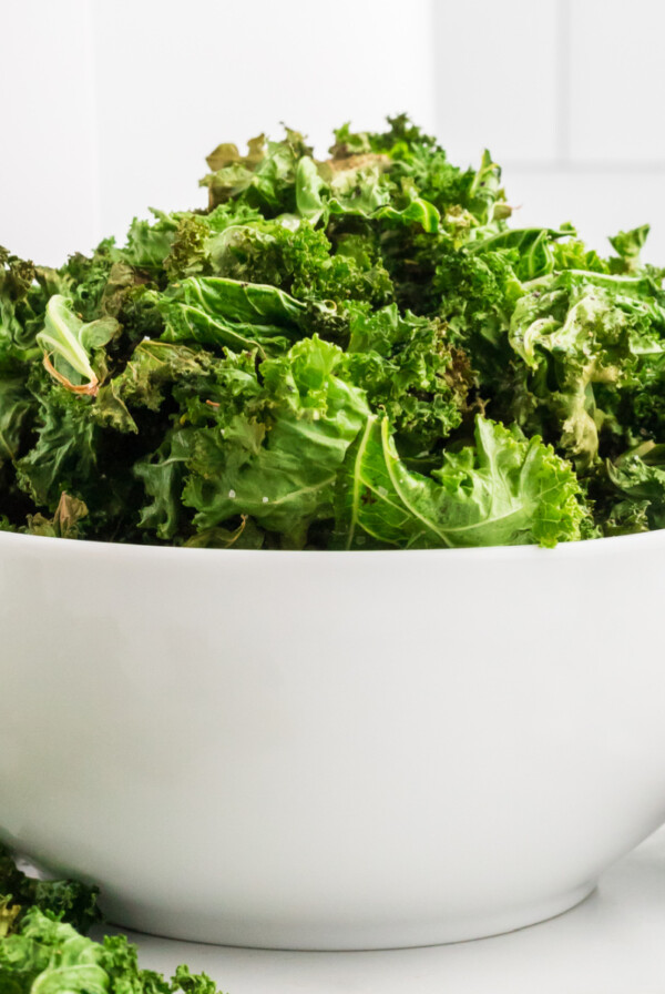 Kale chips are fully cooked in the air fryer and served in a round white bowl.