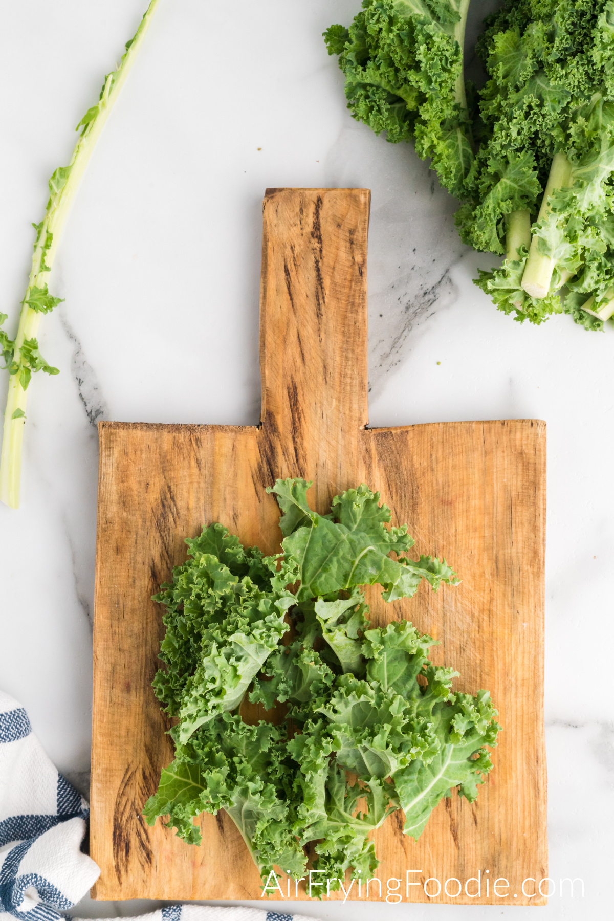 A cutting board with washed, cut-up kale leaves being prepped for cooking in the air fryer. In the top right of the picture is more kale.