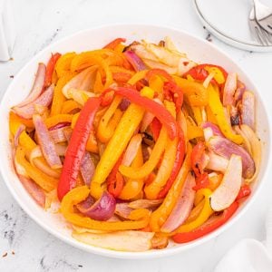 A close-up picture of peppers and onions cooked in the air fryer and served in a round white bowl.