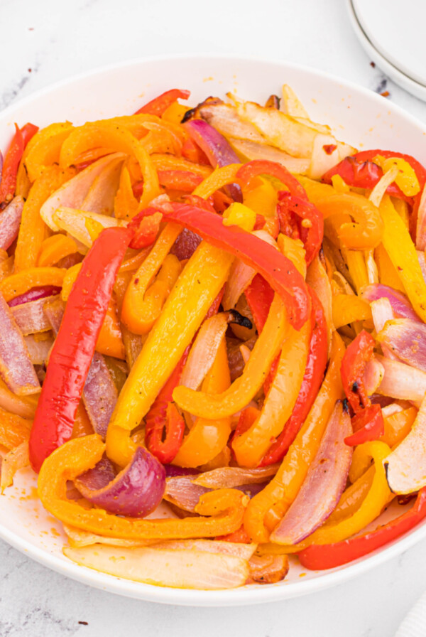 A close-up picture of peppers and onions cooked in the air fryer and served in a round white bowl.