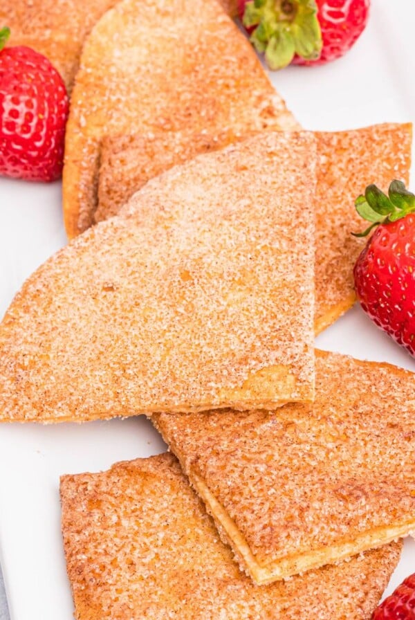 Cinnamon and sugar coated tortilla chips on a white plate with fresh strawberries