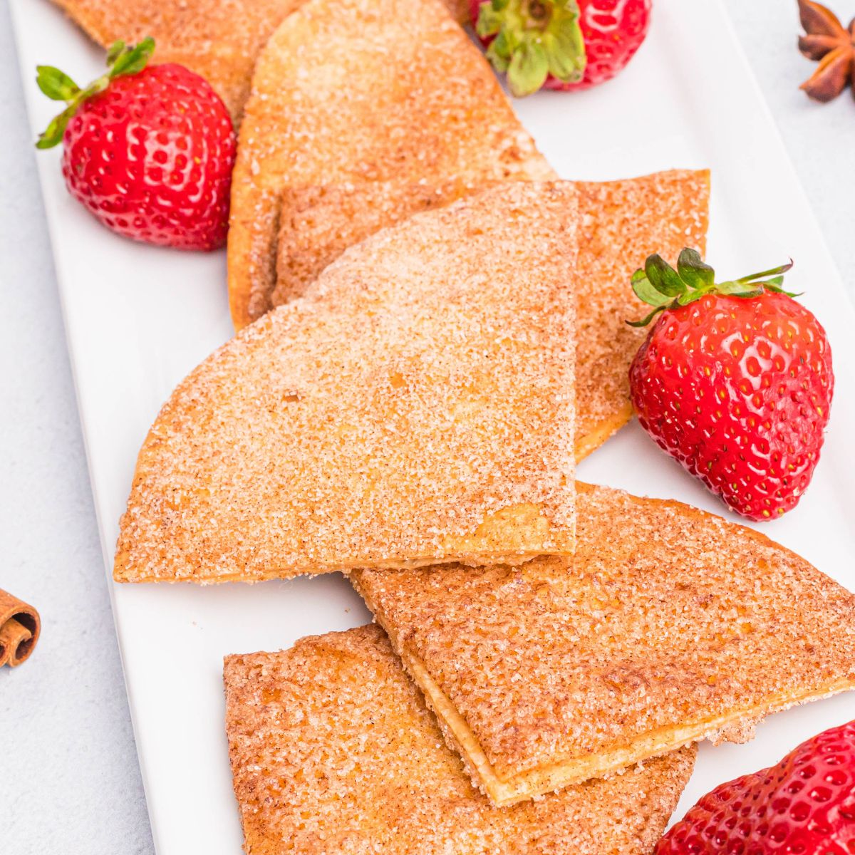 Cinnamon and sugar coated tortilla chips on a white plate with fresh strawberries