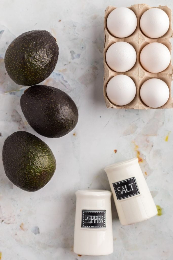 Ingredients to make avocado eggs on a marble table.