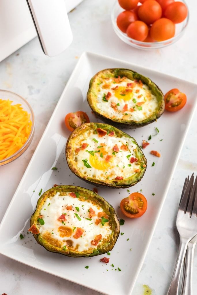 Juicy avocados filled with fried eggs on a white square plate. 
