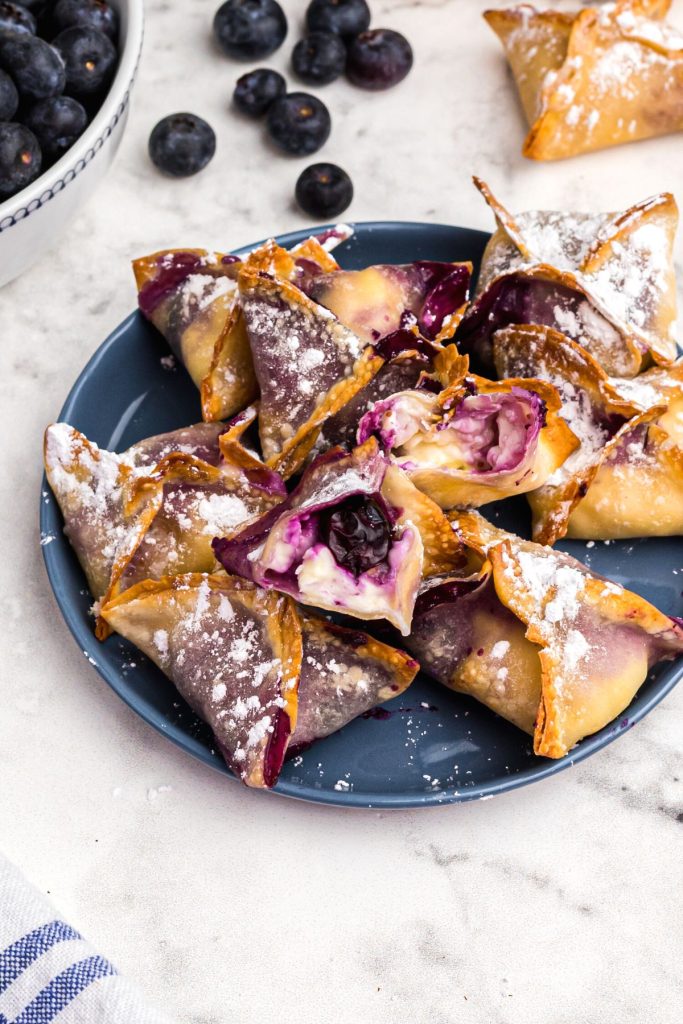 Golden wontons filled with cream cheese and blueberry filling on a blue plate. 