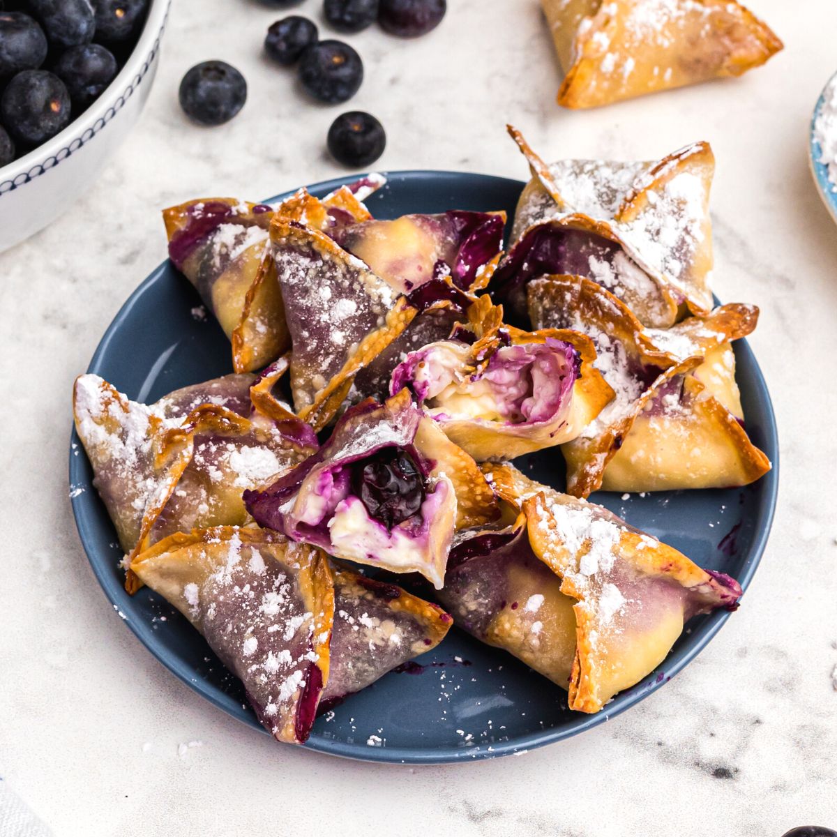 Crispy golden wontons filled with blueberry cheesecake filling on a blue plate.