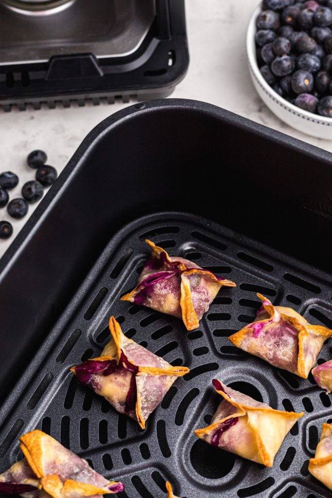 Golden crispy wontons filled with cream cheese cheesecake in the air fryer basket. 