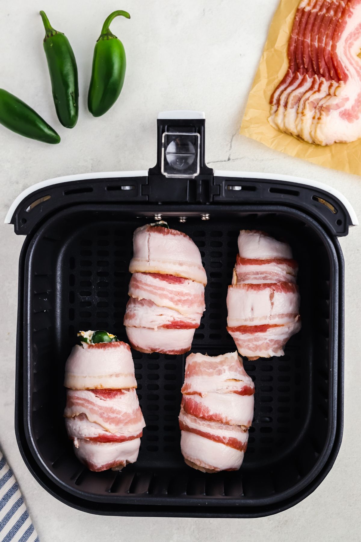 Bacon wrapped chicken and jalapeno poppers in the air fryer basket before being cooked