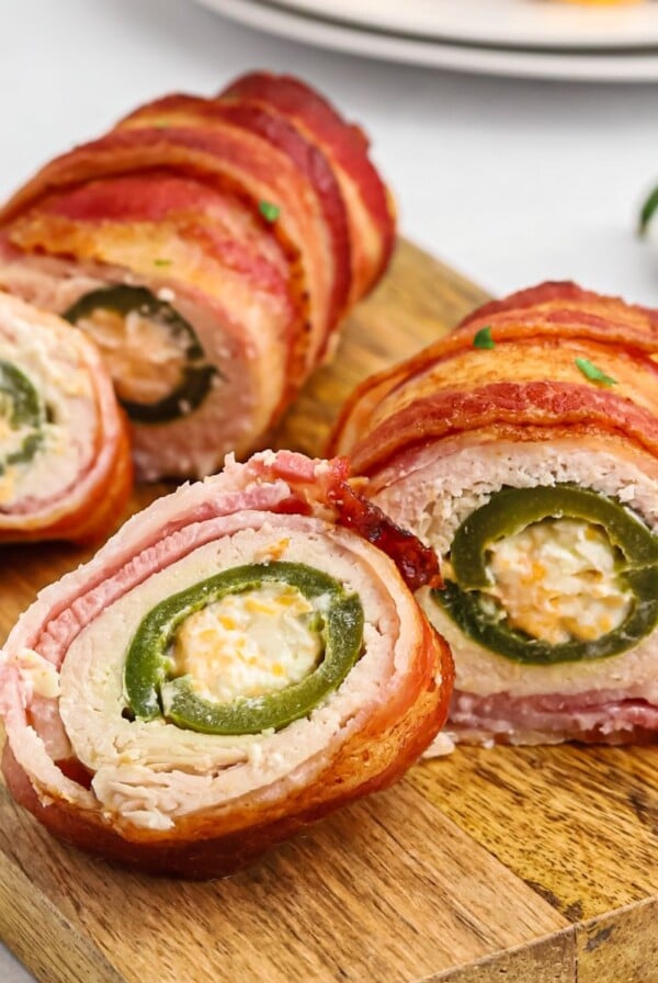 Crispy bacon wrapped around chicken, wrapped around jalapeno poppers on a wooden cutting board.