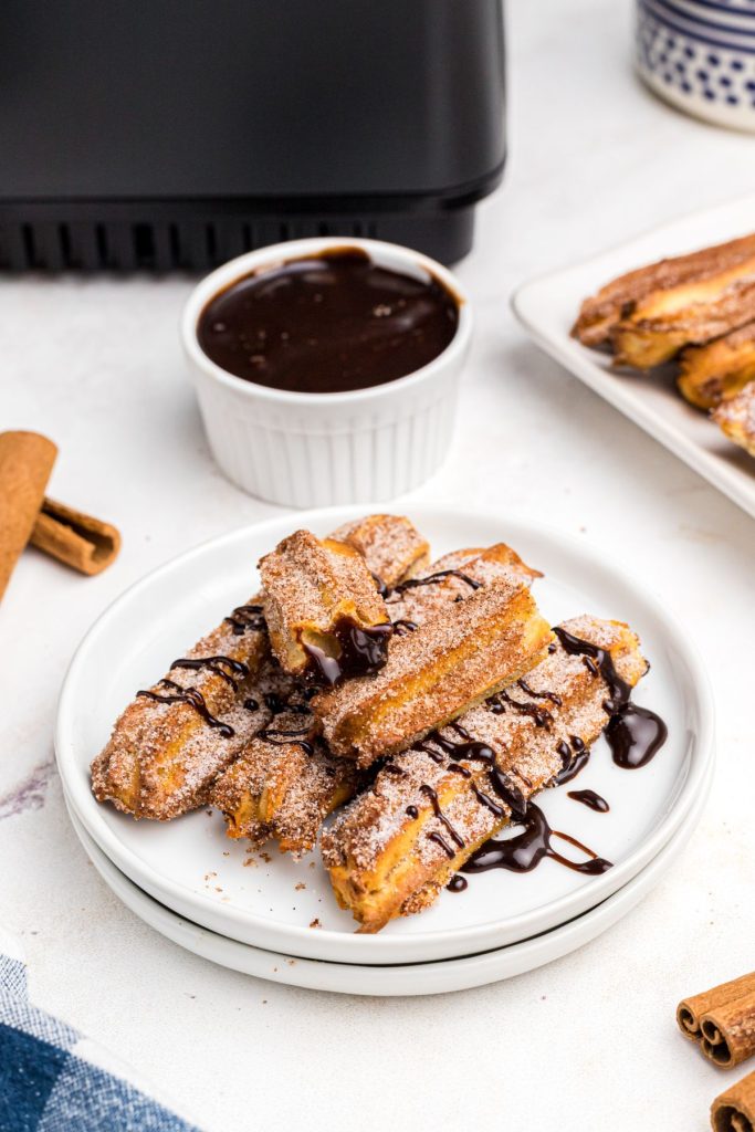 Golden crispy sugar coated churros on a white plate then drizzled in chocolate