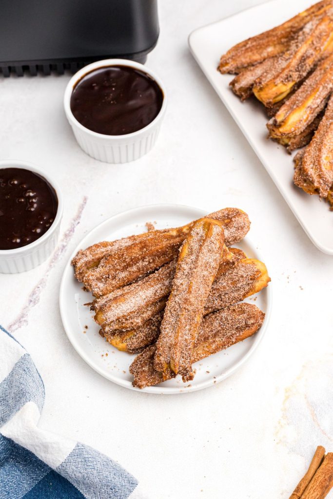 Golden sugar and cinnamon coated churros on a white plate with chocolate sauce