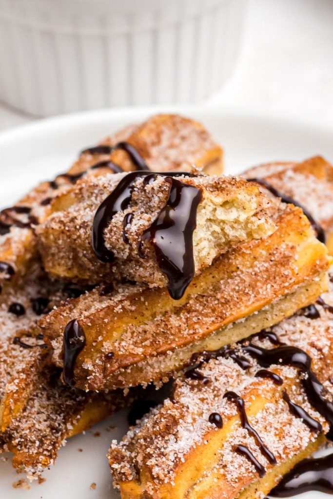 Golden crispy churros on a white plate with melted chocolate dip