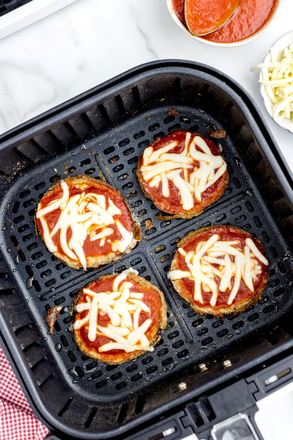 Crispy eggplant sliced with marinara sauce and cheese topped in the air fryer basket after melting cheese in the air fryer