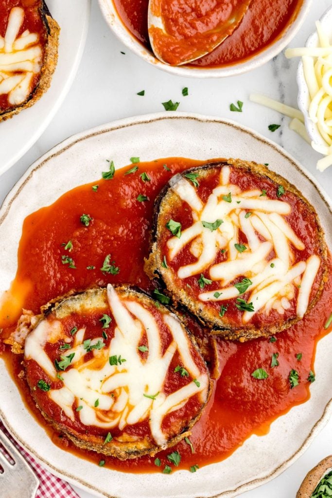 Eggplant slices covered in marinara sauce and parmesan cheese on a white plate